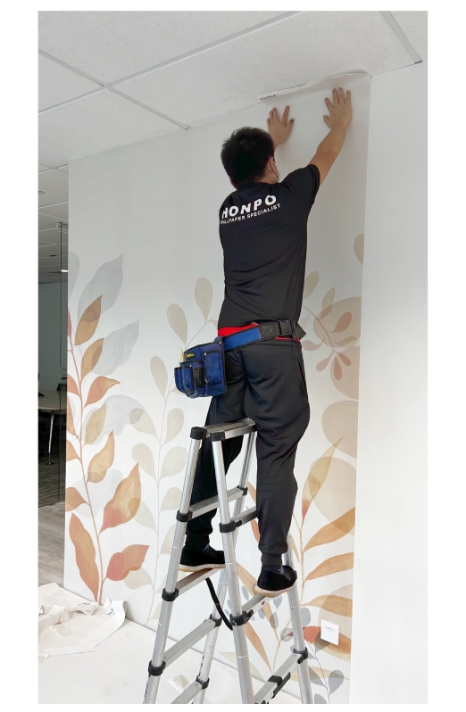 Honpo wallpaper professional installer on a ladder applying botanical-themed wallpaper at the top of the wall